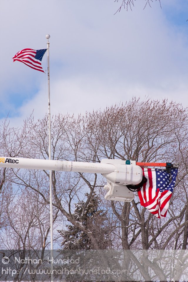 Two flags fly, one from a flagpole, one from a cherry picker